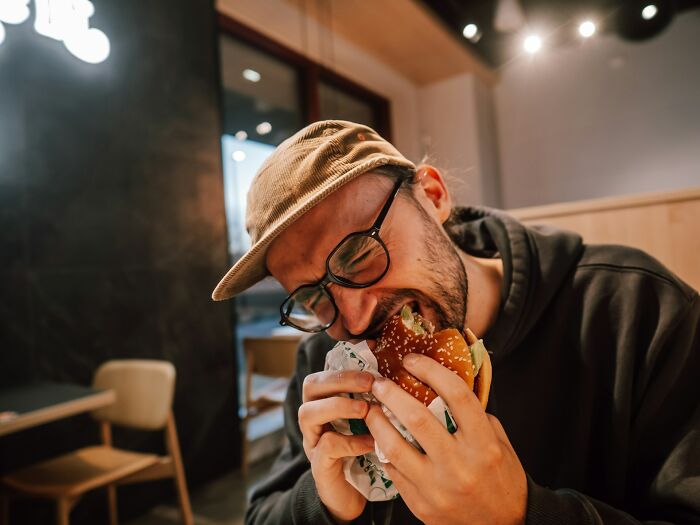 A man with glasses and a cap taking a large bite out of a burger, representing ridiculous things people said.