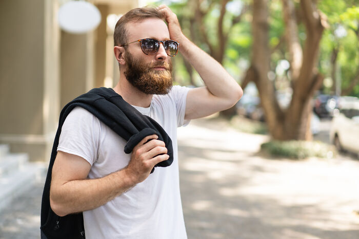 Man wearing sunglasses outdoors with jacket over shoulder