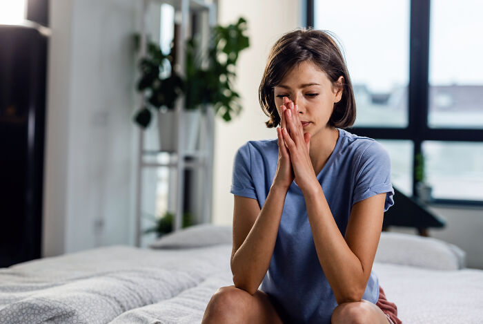 A sad, reflective woman sitting on a bed, representing the feelings of divorced people