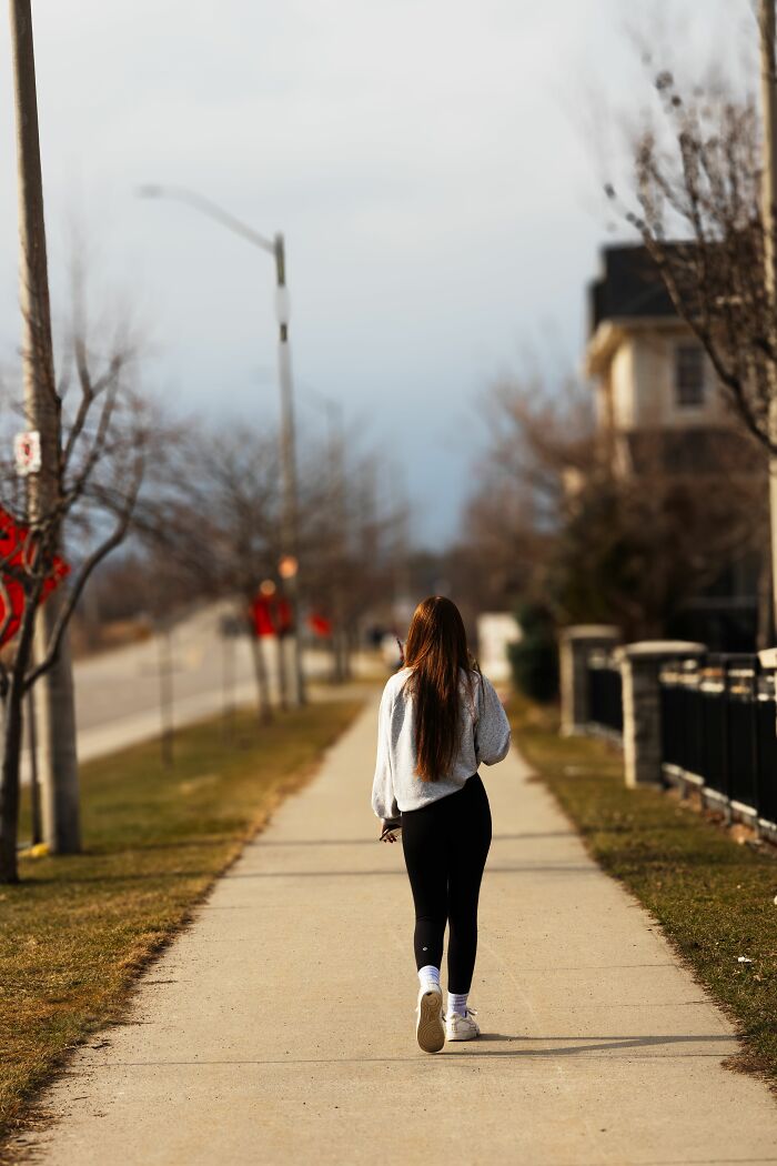 A person walking away on a sidewalk, possibly having a 6th sense about something ahead.