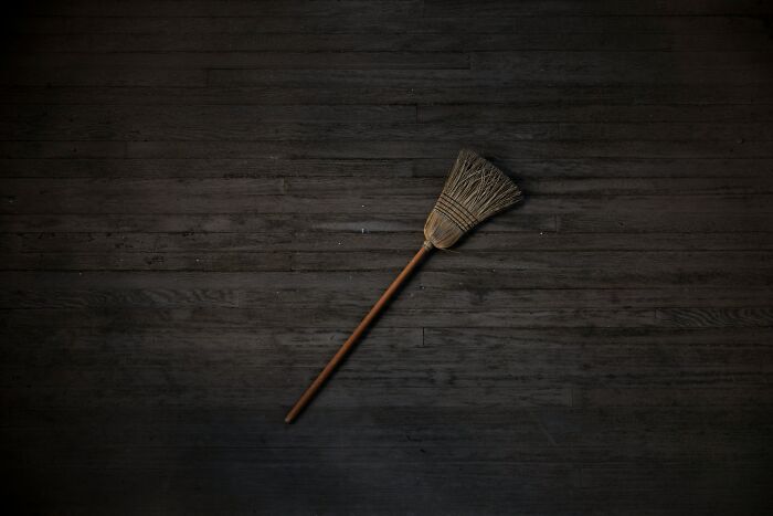 A single broom on a dark wooden floor. Someone's sixth sense smells a rat about the broom.