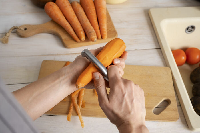 Hands peeling a fresh carrot on a cutting board in a kitchen