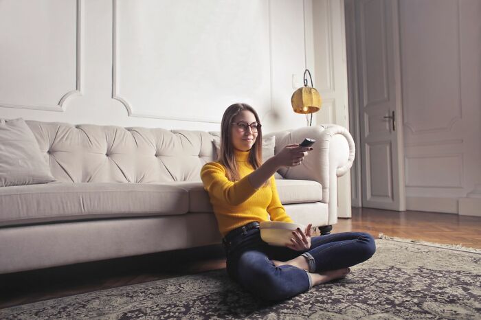 A woman sitting on the floor, holding a bowl and a remote, watching TV, coping with relationships ending.