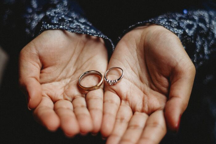 Two hands cupped together hold a wedding band and an engagement ring, symbolizing relationships.