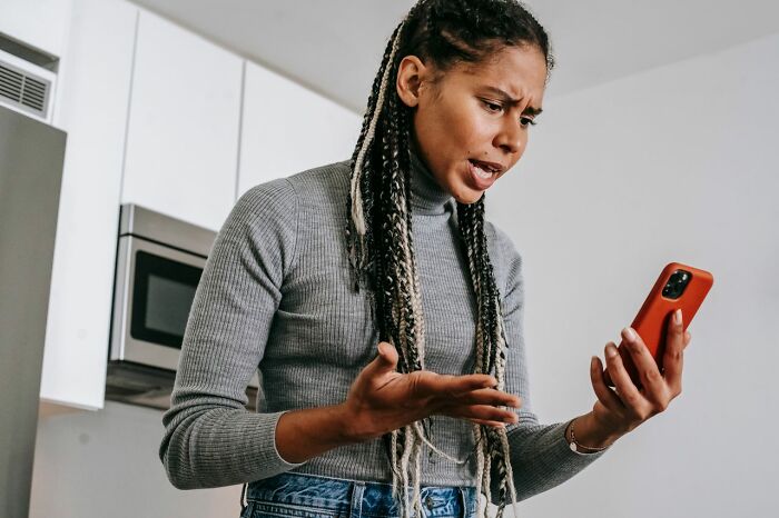 A woman looking upset while holding a phone, demonstrating savage things people did after relationships fell apart.