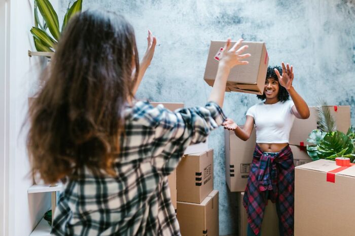 Two women playfully tossing a moving box, illustrating things people did after their relationships fell apart.