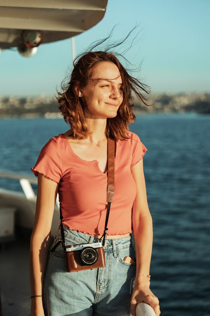 A woman with wind-swept hair and a camera around her neck, smiling while on a boat, representing things people did after their relationships fell apart.