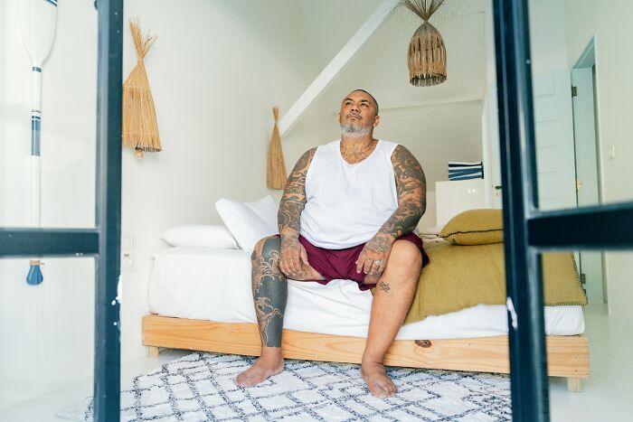 A man with many tattoos sitting on a bed, looking up, reflecting things people did after their relationships fell apart.