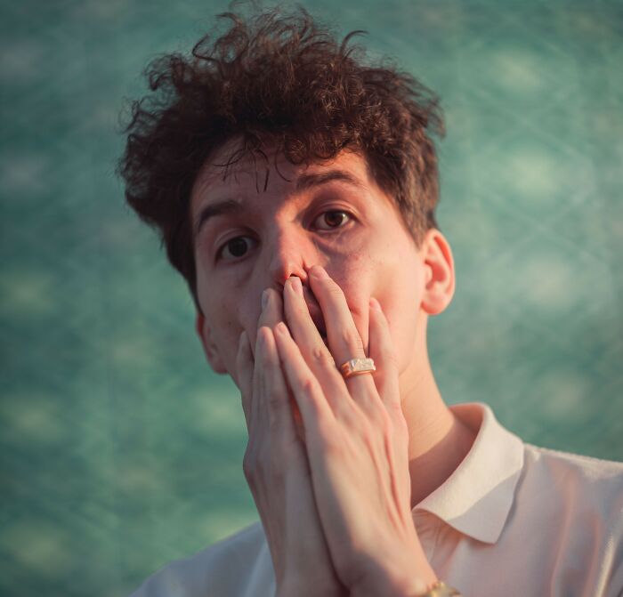 A young man looking shocked while covering his mouth with his hands