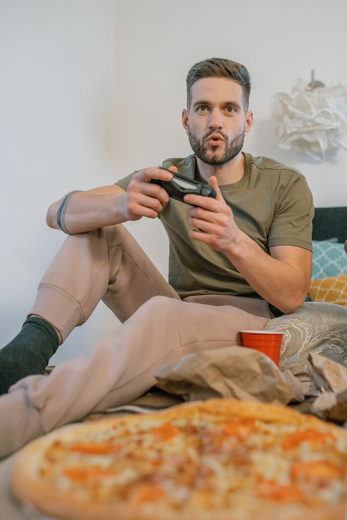 A man playing video games in bed with pizza, an example of unserious dating red flags.