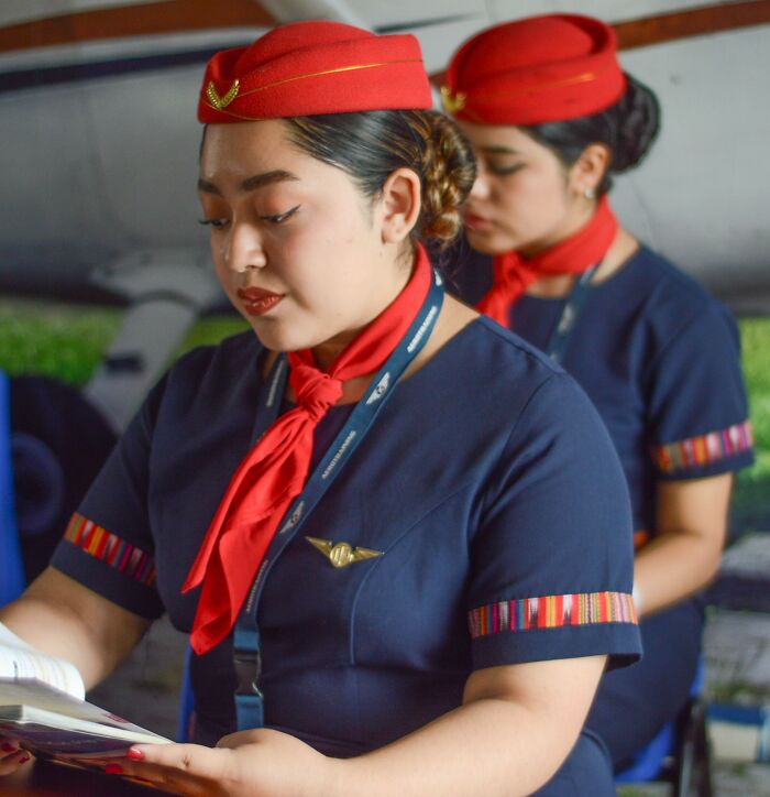 Two flight attendants in uniform read a manual, maintaining a professional image free of scandals.
