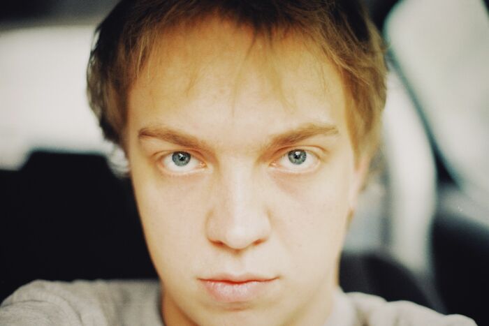 A young man with light hair and piercing blue eyes, exhibiting traits of a sociopath.