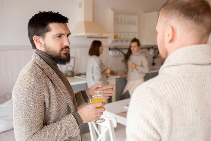 Two men talking, one holding a drink, illustrating dating red flags in a social setting.