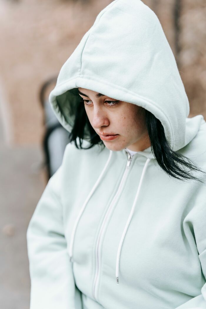 A young woman in a light hoodie looks down, symbolizing children who are going through difficult experiences.