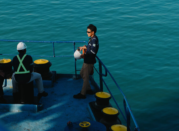 Two men on a boat, one looking out at the sea, illustrating people who overheard something.