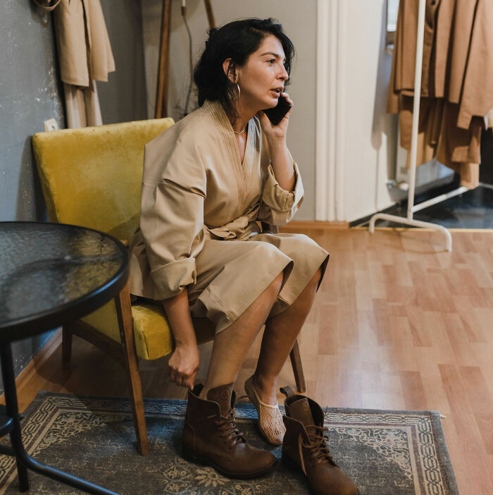 A woman sits on a yellow chair, talking on a phone, perhaps overhearing something not meant for her.