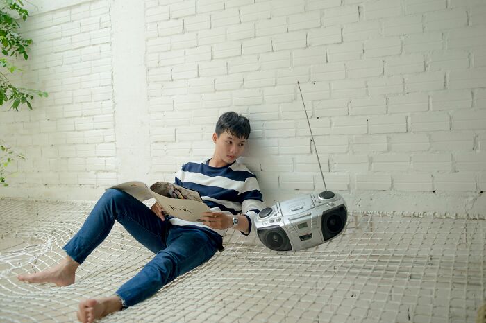 A man sitting on a hammock with a boombox and reading, evoking childhood beliefs.