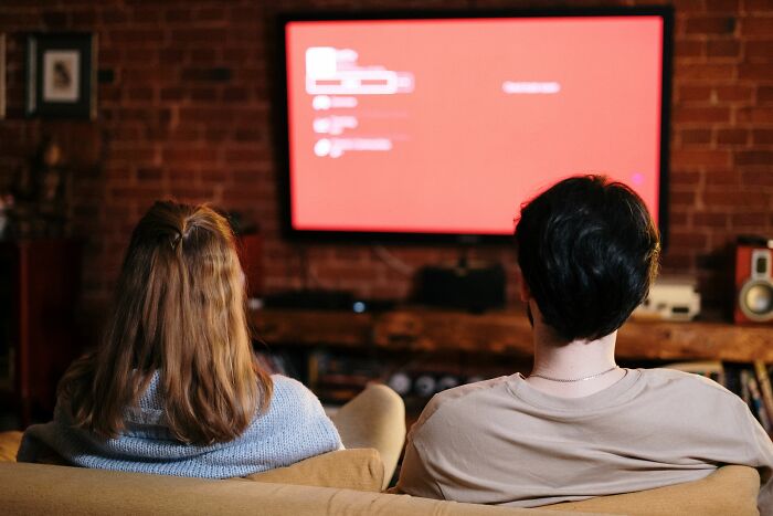 A couple watching a red screen on TV, illustrating scandals that should have had someone cancelled.