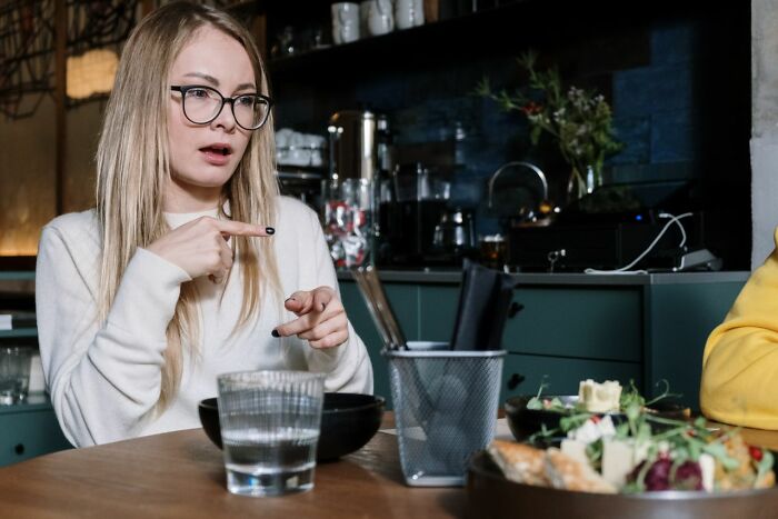 A woman wearing glasses points while enjoying delicious dinner and hot tea at a restaurant table.