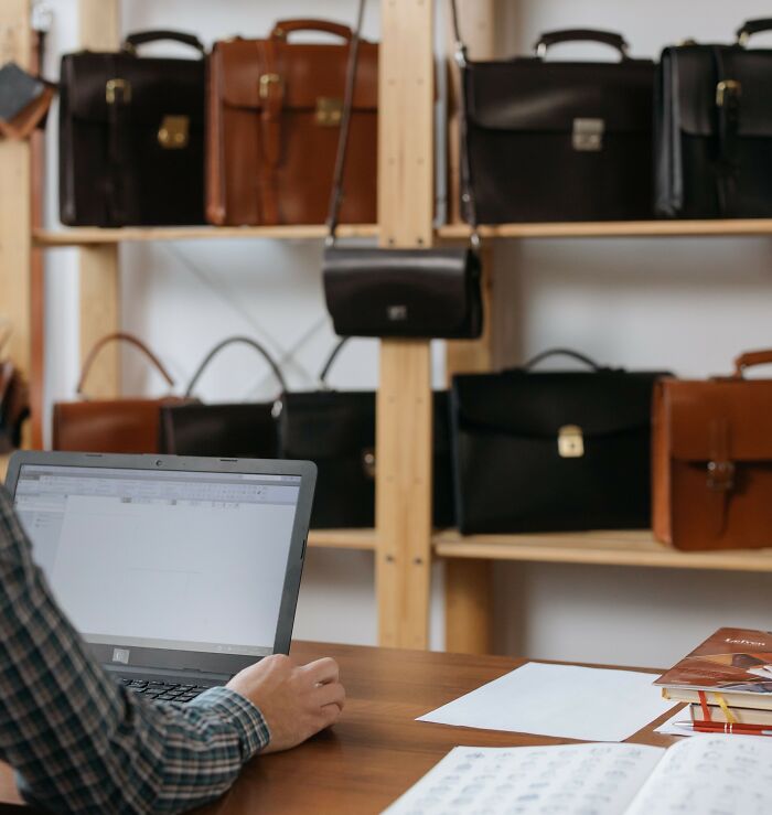 A person using a laptop in front of leather briefcases, representing rich people luxury