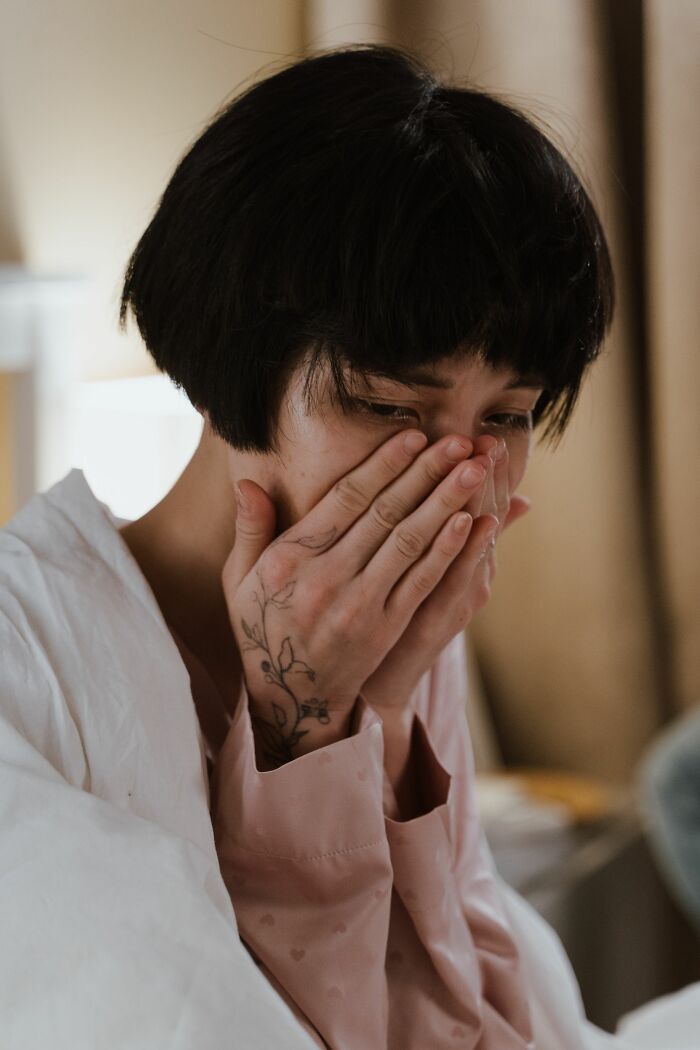 A person with short dark hair covering their face with their hands, appearing upset, highlighting something people overheard.