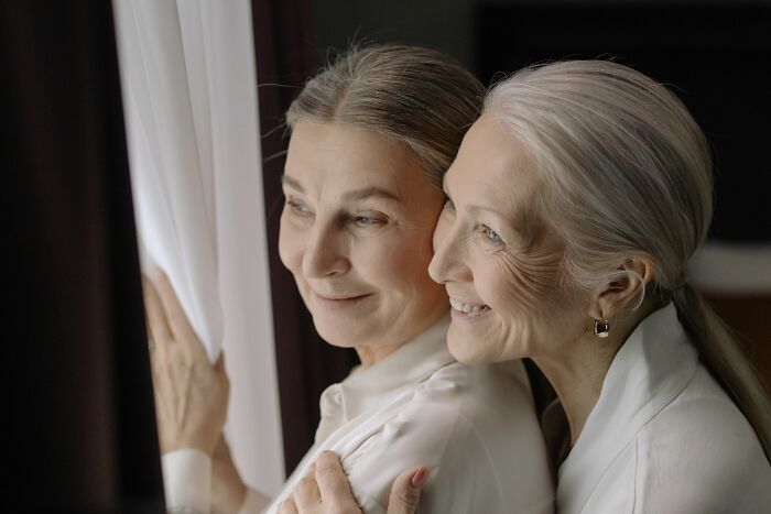 Two older women smiling and looking out a window, sharing moments as secrets came to light.
