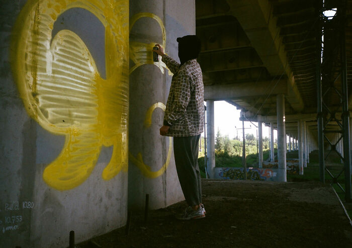 A person spray painting a concrete pillar under an overpass, reflecting the brutal response of fence builders. A person spray painting a concrete pillar under an overpass, reflecting the brutal response of fence builders.
