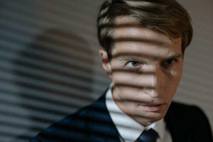 A man with intense eyes, partially shadowed by blinds, portrays the unsettling gaze of a potential sociopath.