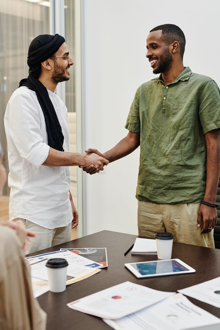 Two men shaking hands in a business setting, representing a stereotype about the US.