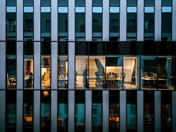 Modern office windows at night showing desks and chairs, a place where corporate scandals might arise.