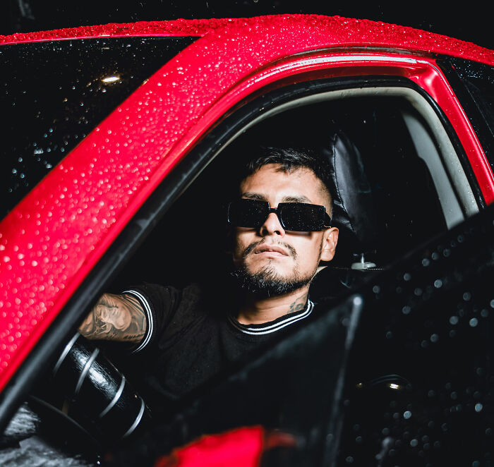 A man in sunglasses and a black t-shirt sits in a red car during a Becky experiment, testing dating profiles. A man in sunglasses and a black t-shirt sits in a red car during a Becky experiment, testing dating profiles.