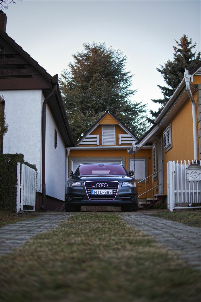 A dark colored car parked in a narrow driveway between two houses. Safety tips for women living alone.