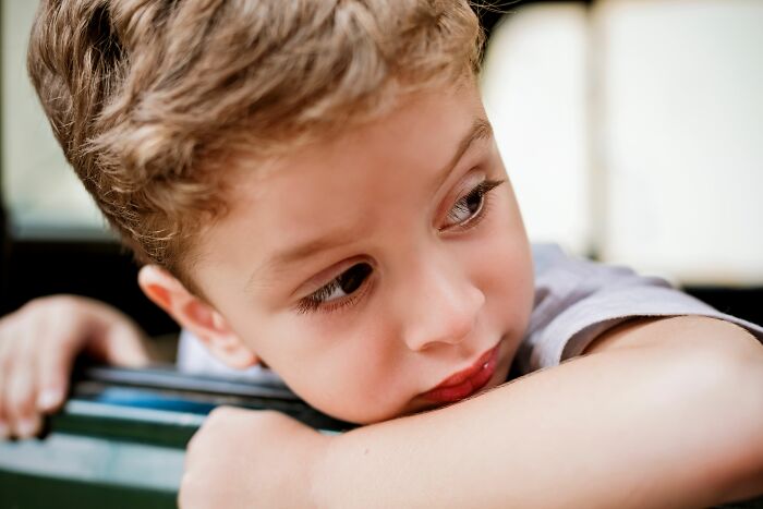 A young child with curly brown hair resting their head on their arm, looking away thoughtfully.