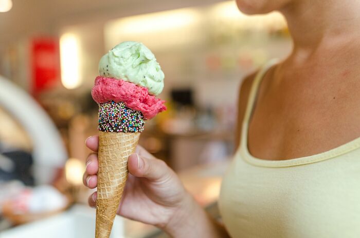 A person holds a colorful triple-scoop ice cream cone, a sweet treat often enjoyed on first dates.
