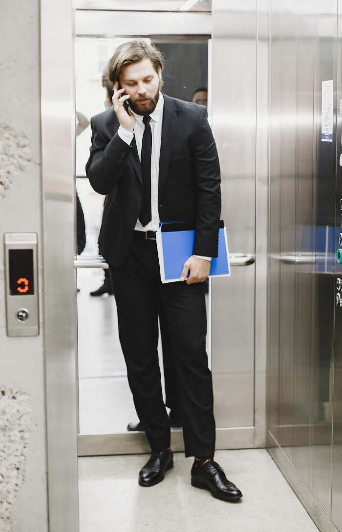 A man in a suit talking on his phone in an elevator, appearing to have overheard something he wasn't meant to hear.