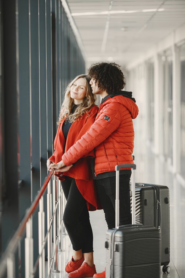 A couple holding hands in an airport, looking out a window, possibly after people overheard something.