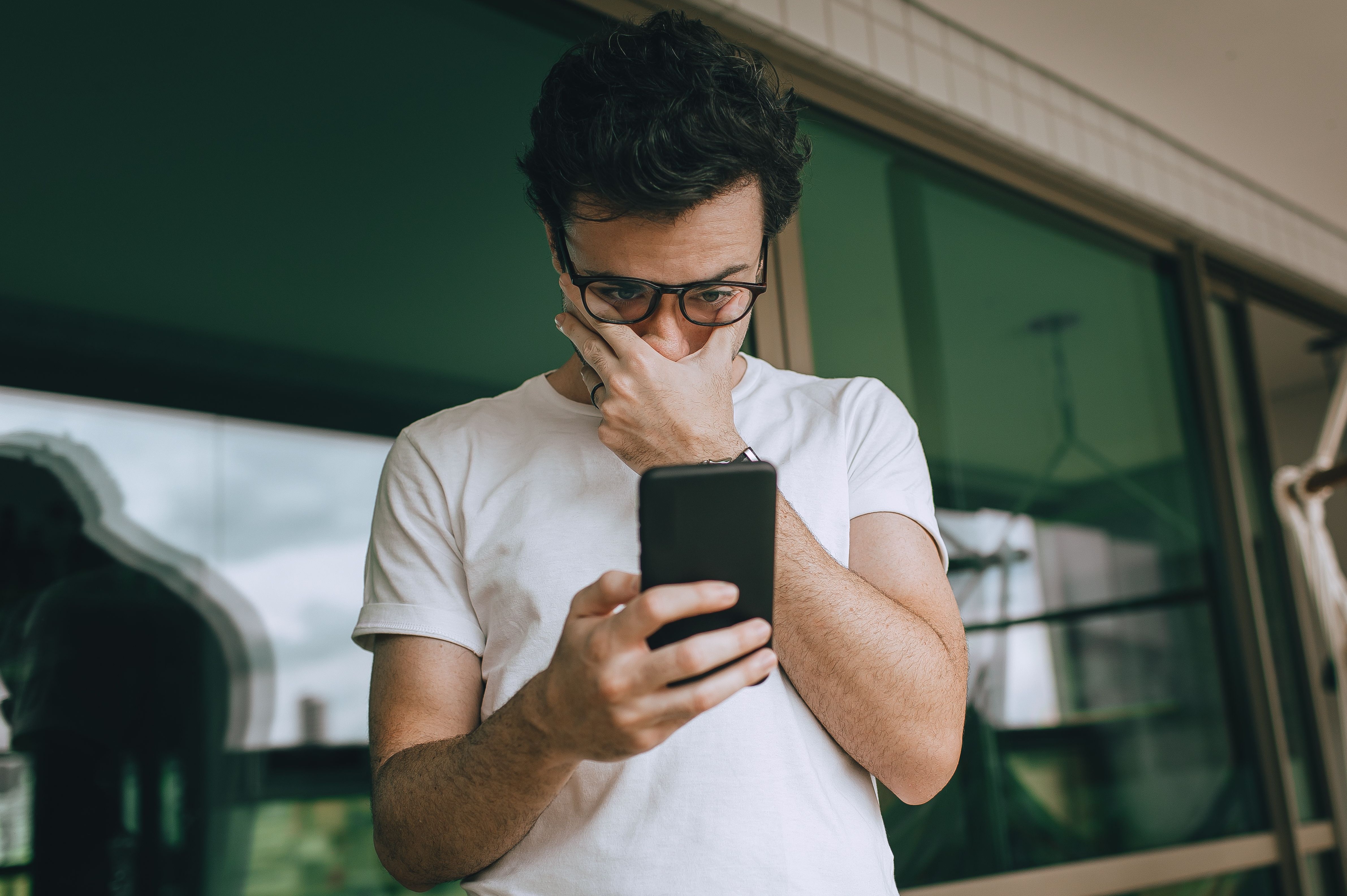 Worried man looking at his smartphone, concerned about credit card thief activity