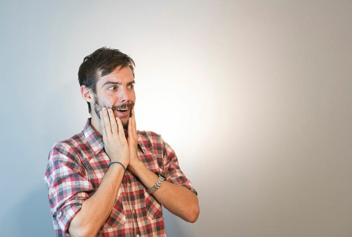 Bearded man with hands on face, looking amazed, perhaps at a delicious dinner or hot tea.