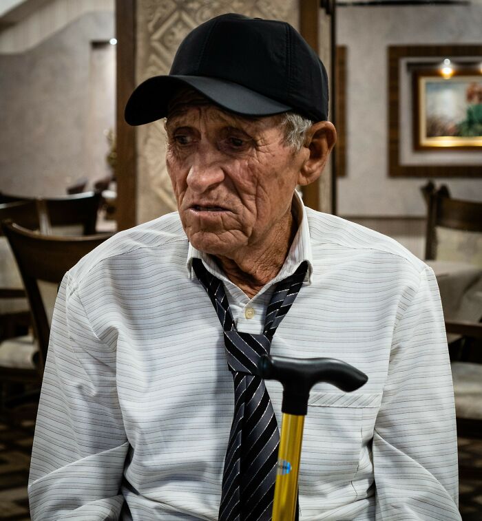Elderly man with cane and hat sitting in restaurant looking sideways