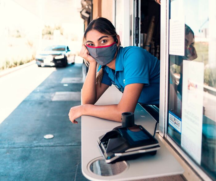 Masked restaurant worker leaning out of drive-thru window