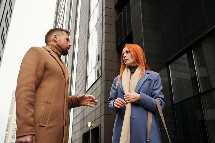 A man and a woman talking outdoors in front of a modern building, discussing dating red flags.