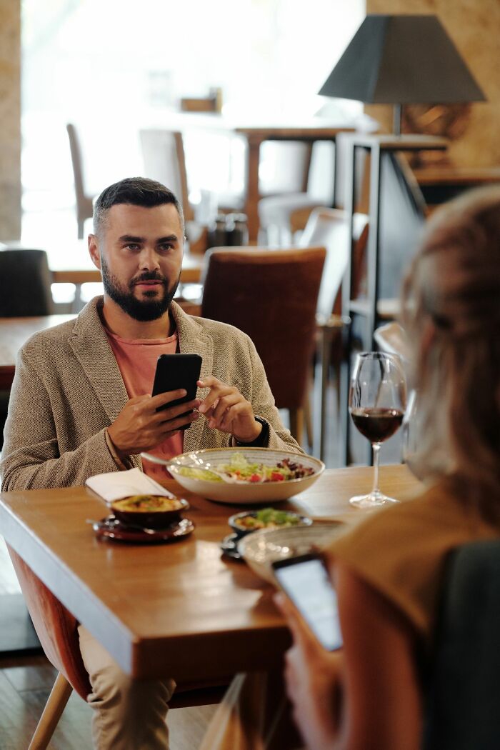 Man waiting to be served delicious dinner and hot tea at a restaurant, looking at his phone.
