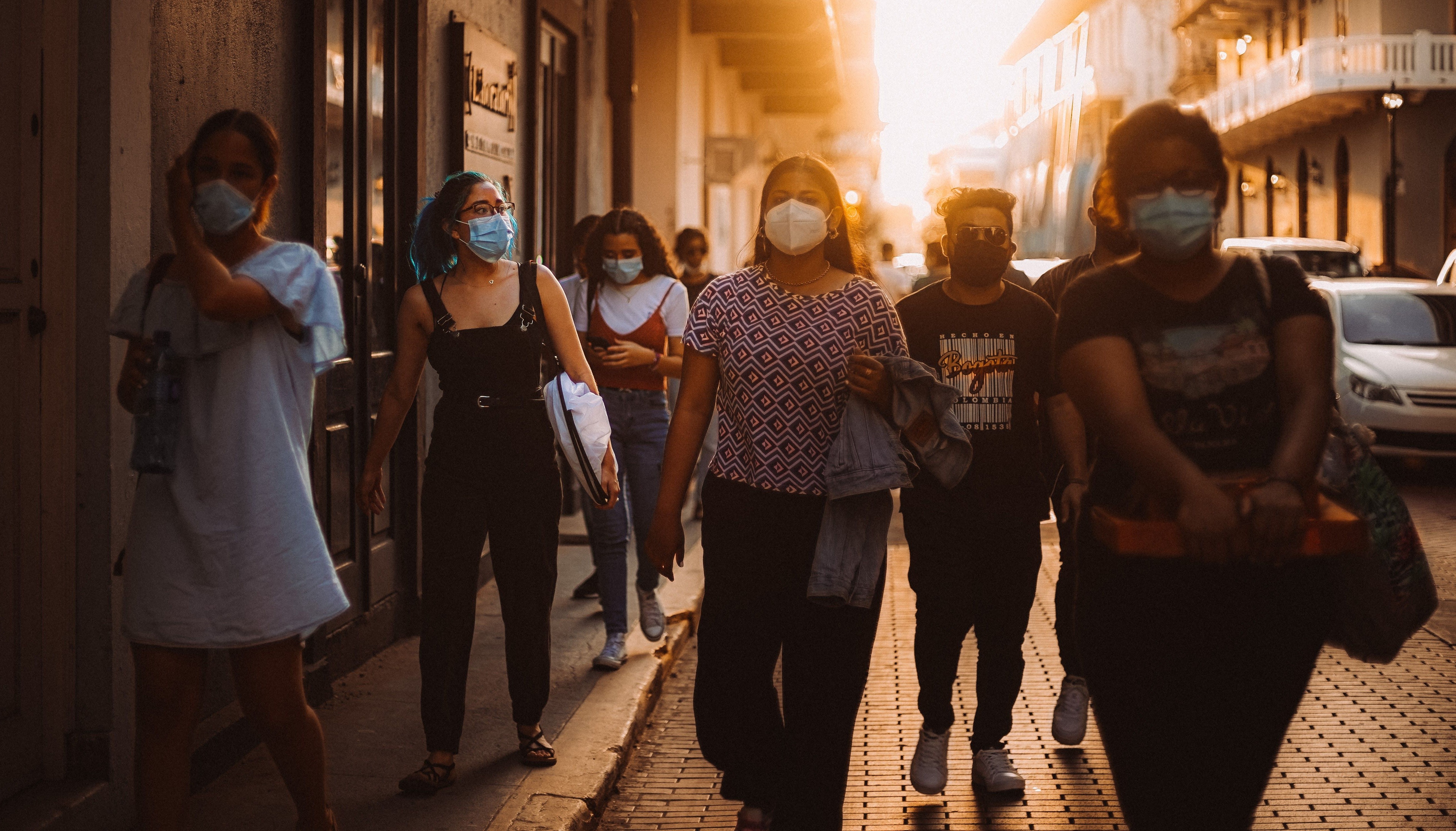 Group of people walking on street wearing face masks at sunset