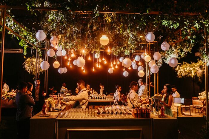 An outdoor wedding reception bar illuminated by hanging warm globe lights during evening weddings