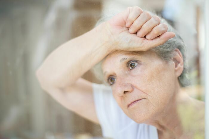 An older woman looking out a window with a worried expression, reflecting on health symptoms that terrify doctors.