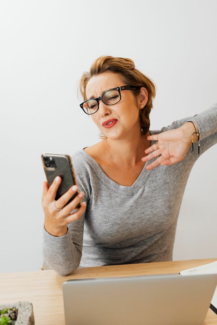 A woman wearing glasses looks at her phone with a disgusted expression, showing potential dating red flags on her screen.