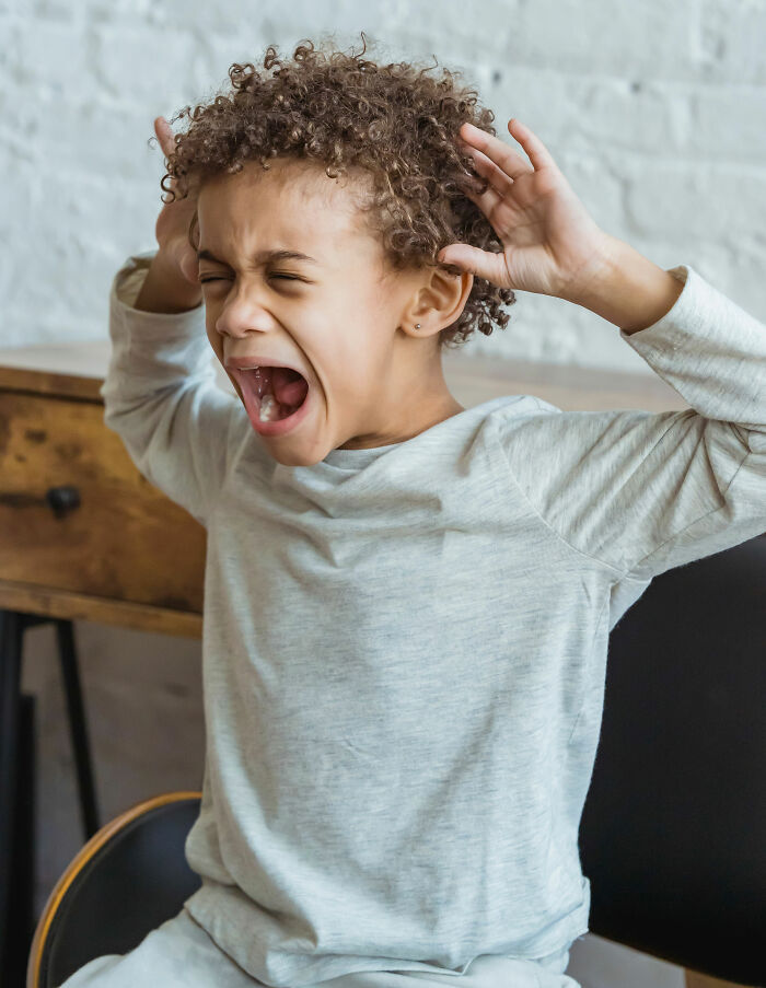 A young boy with curly hair screaming and holding his head, depicting someone who overheard something surprising.