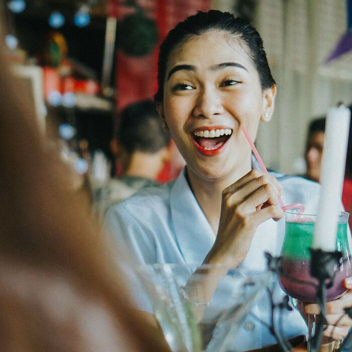 Woman laughing and drinking colorful cocktail at restaurant enjoying funny moment