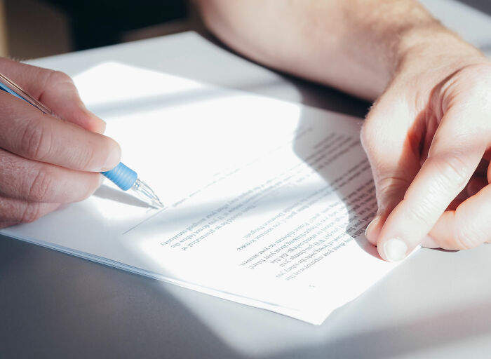 A person's hand holding a pen, signing a document, symbolizing the legal or contractual aspects for fence builders. A person's hand holding a pen, signing a document, symbolizing the legal or contractual aspects for fence builders.