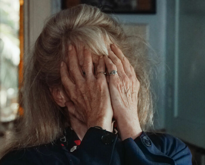 Older woman covering her face showing distress in family boundary conflict Older woman covering her face showing distress in family boundary conflict
